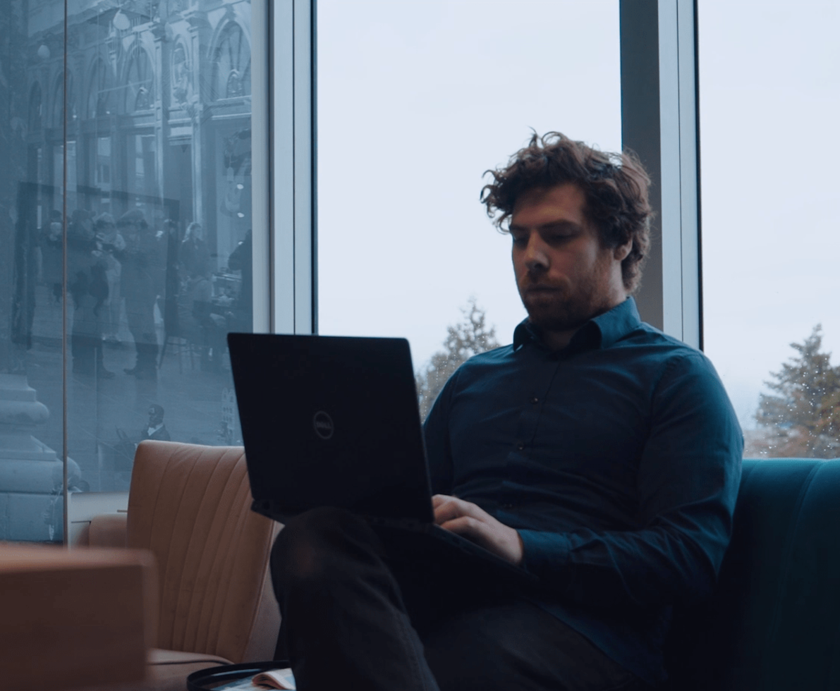 Photo of a man working on his laptop while sitting in a sofa.